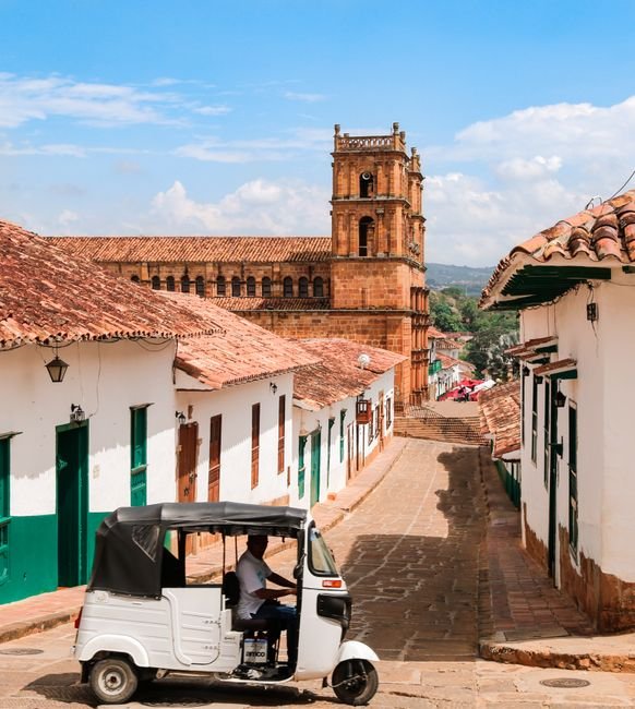 Tuk-tuk passing colonial church on a cobblestone street in Barichara, Colombia