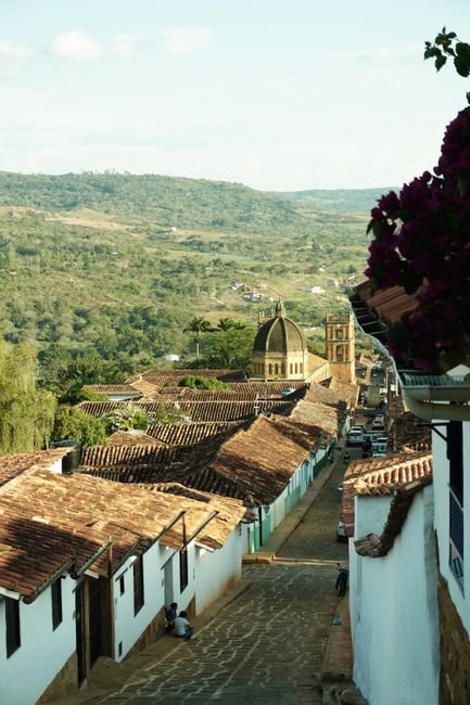 Cobblestone street in Barichara with ochre stone colonial buildings, bougainvillea, and the Andes visible in the background