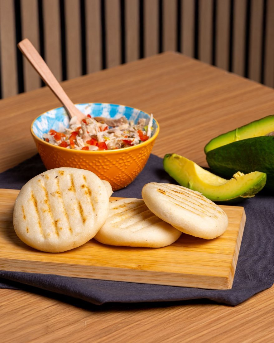 Grilled arepas with shredded chicken and sliced avocado on a wooden board