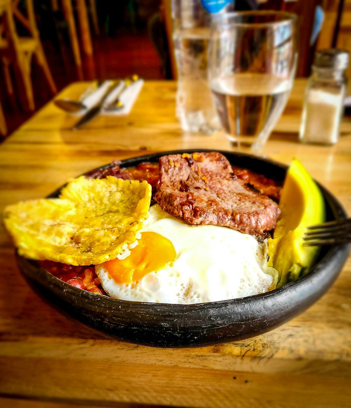 Colombian plate with steak, fried egg, plantain and avocado in a black bowl, Bogota