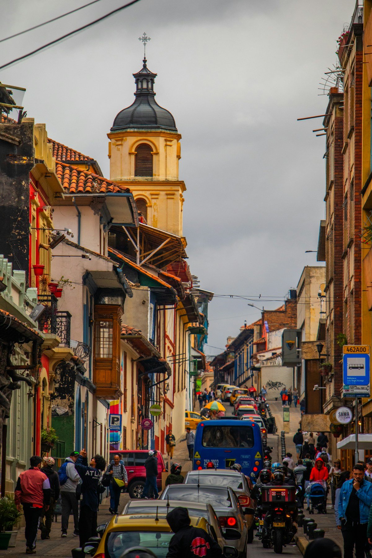Busy colonial street in La Candelaria Bogota with yellow taxis and church tower in background
