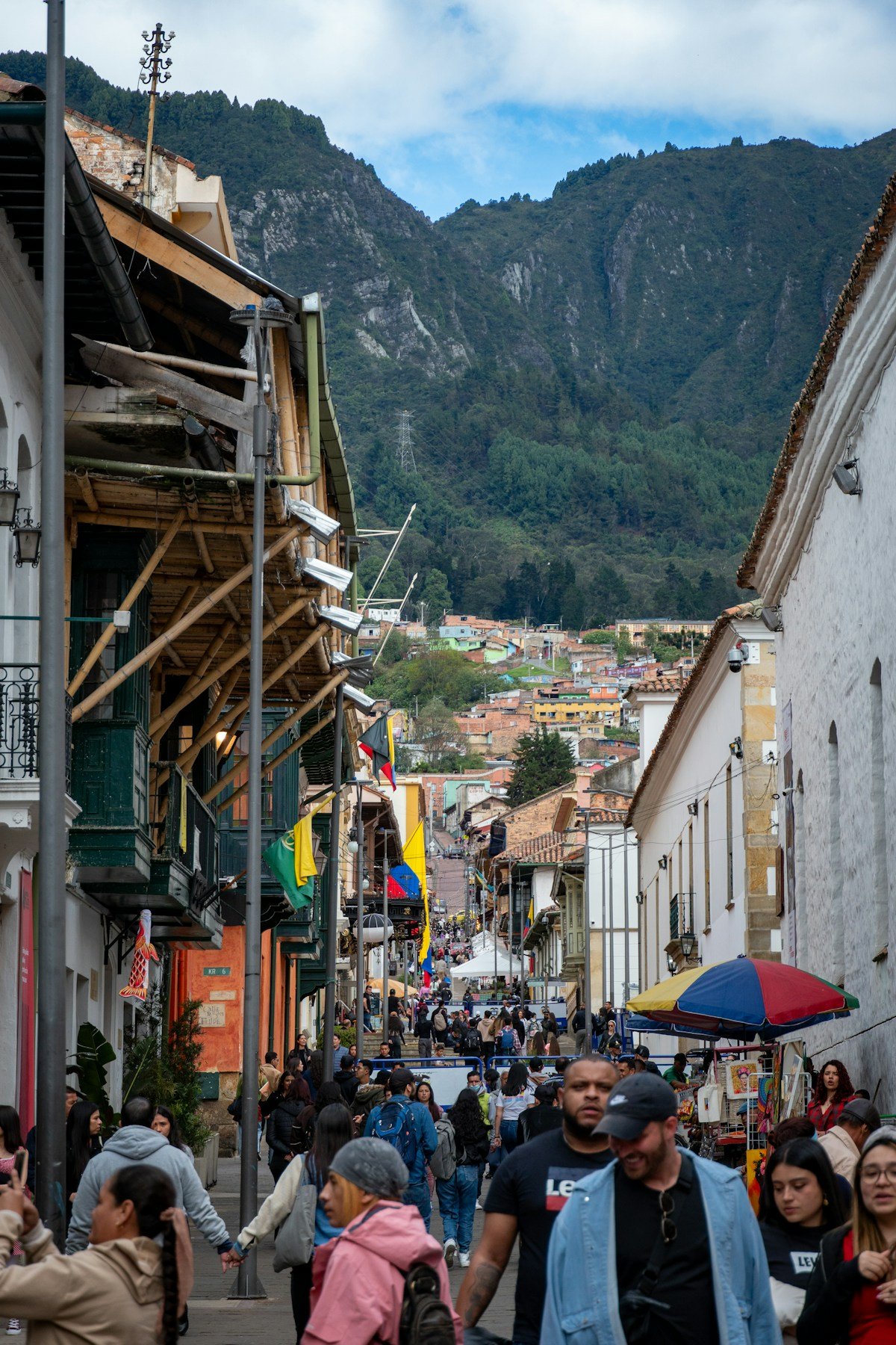 Busy pedestrian street in La Candelaria, Bogota, with Monserrate mountain rising behind colonial buildings