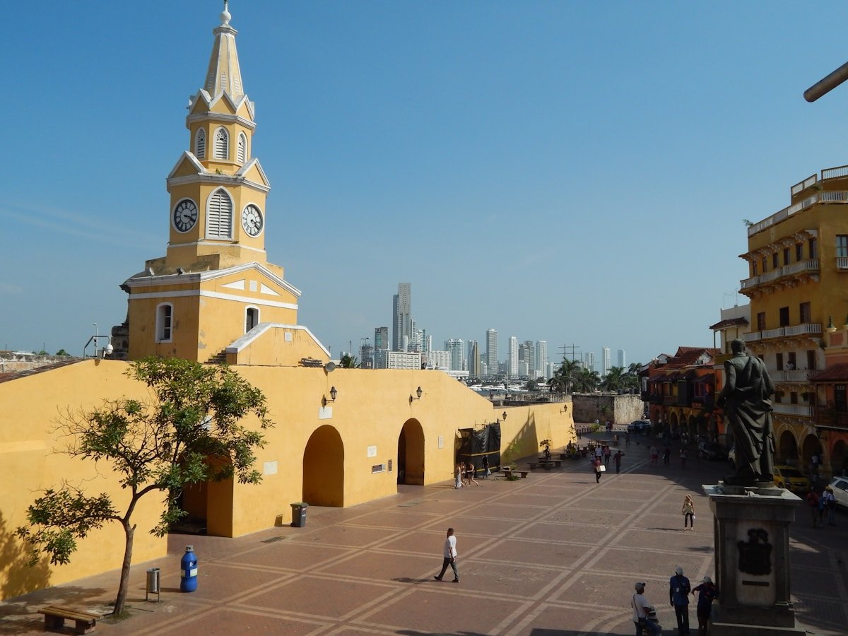 Cartagena's yellow Torre del Reloj clock tower framing the entrance to the walled city with the modern Bocagrande skyline behind