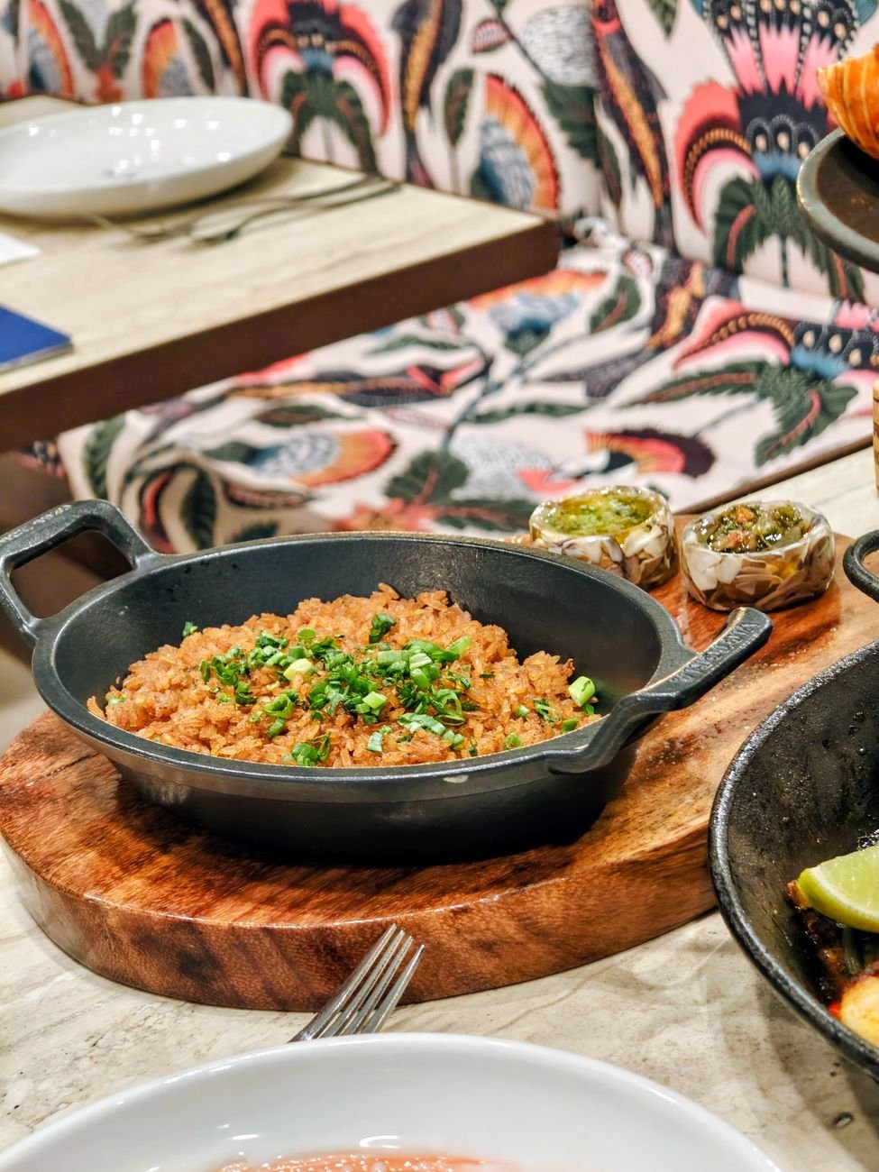 Colombian rice garnished with fresh herbs in a cast iron pan at a Cartagena restaurant, with colourful tropical decor behind