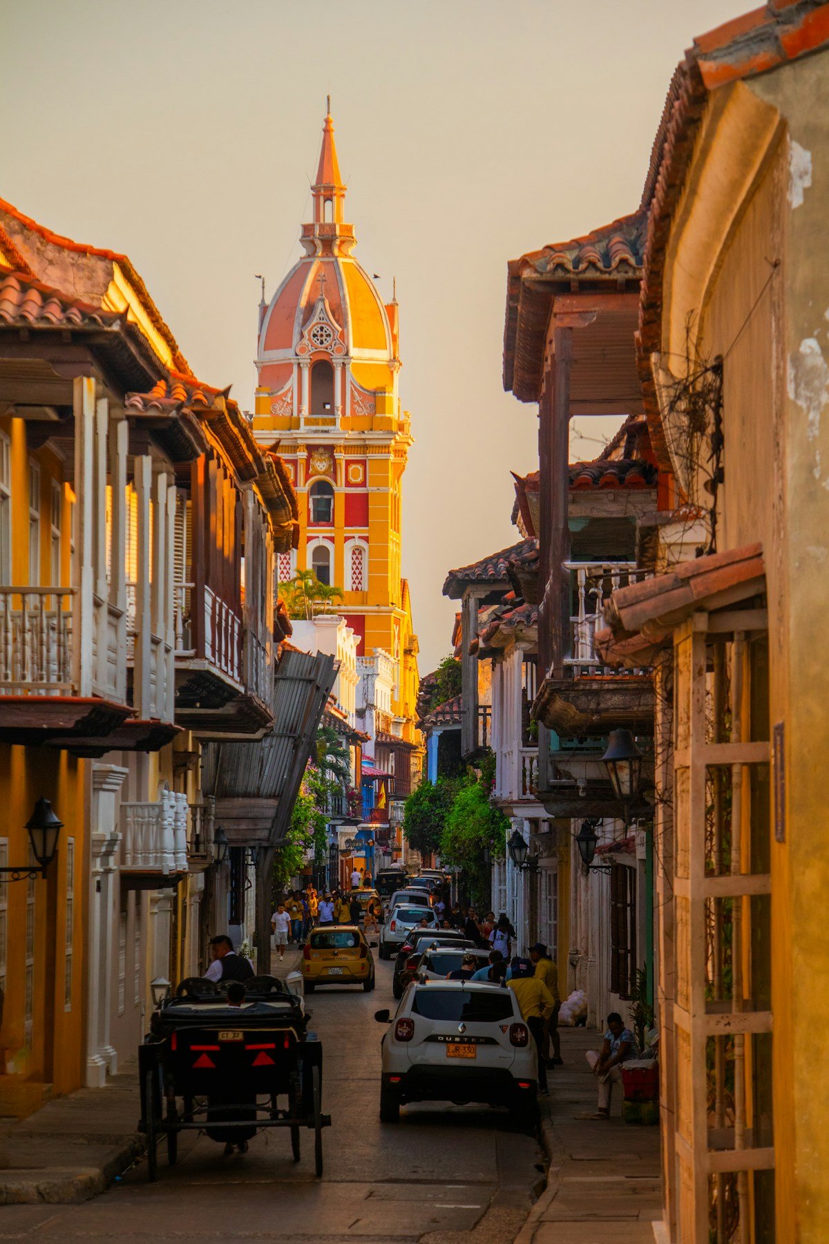 Golden sunset light on colonial street in Cartagena Walled City with cathedral dome rising above balconied buildings