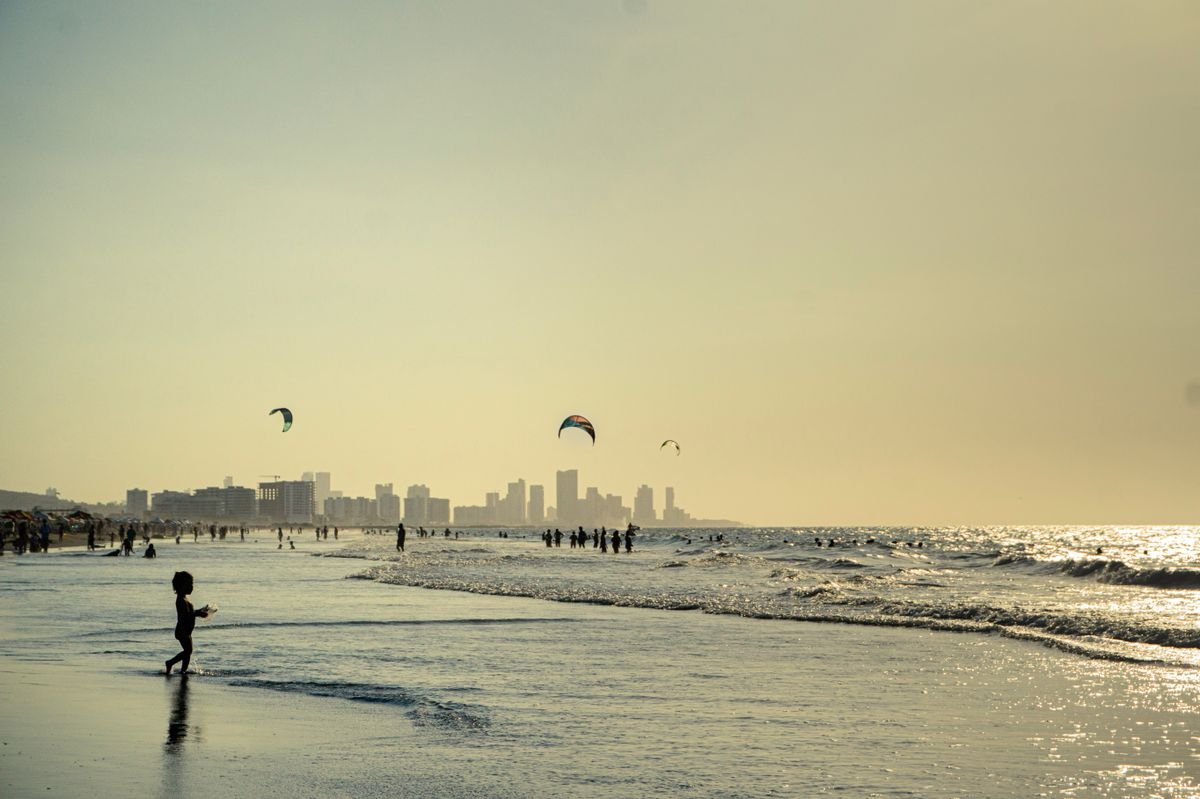 Kitesurfers and beachgoers on a Cartagena beach at golden hour with the skyline behind