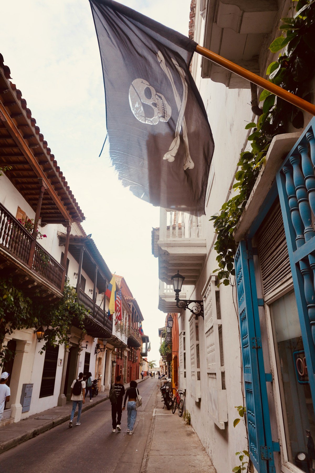 A narrow colonial street in Cartagena's walled city at dusk, with cobblestones and blue painted windows