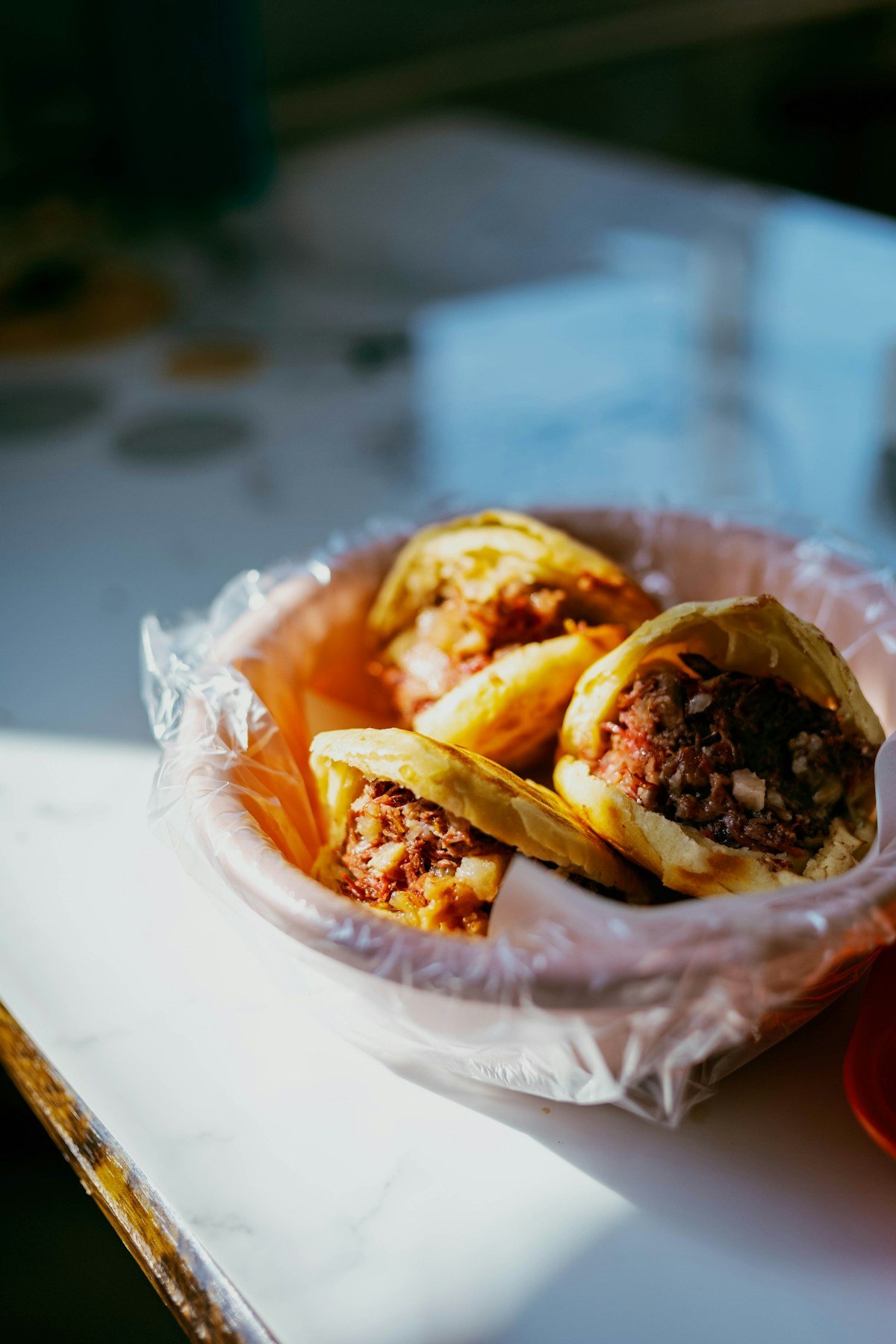 Three arepas filled with meat and beans on a paper plate, Colombia street food