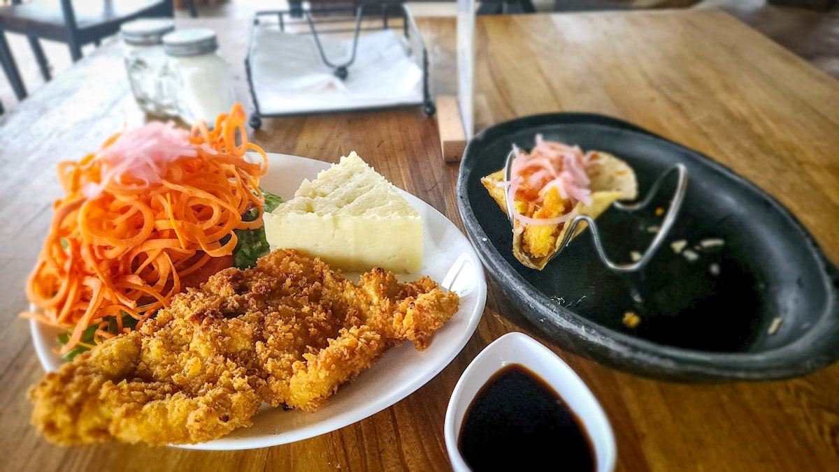 Breaded fish fillet with fresh carrot salad and dipping sauce on wooden table, Minca near Santa Marta, Colombia