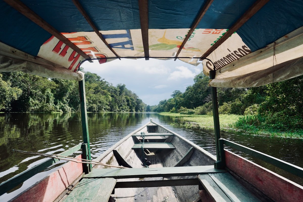 A wooden boat travelling down a wide river surrounded by dense Amazon jungle, Colombia