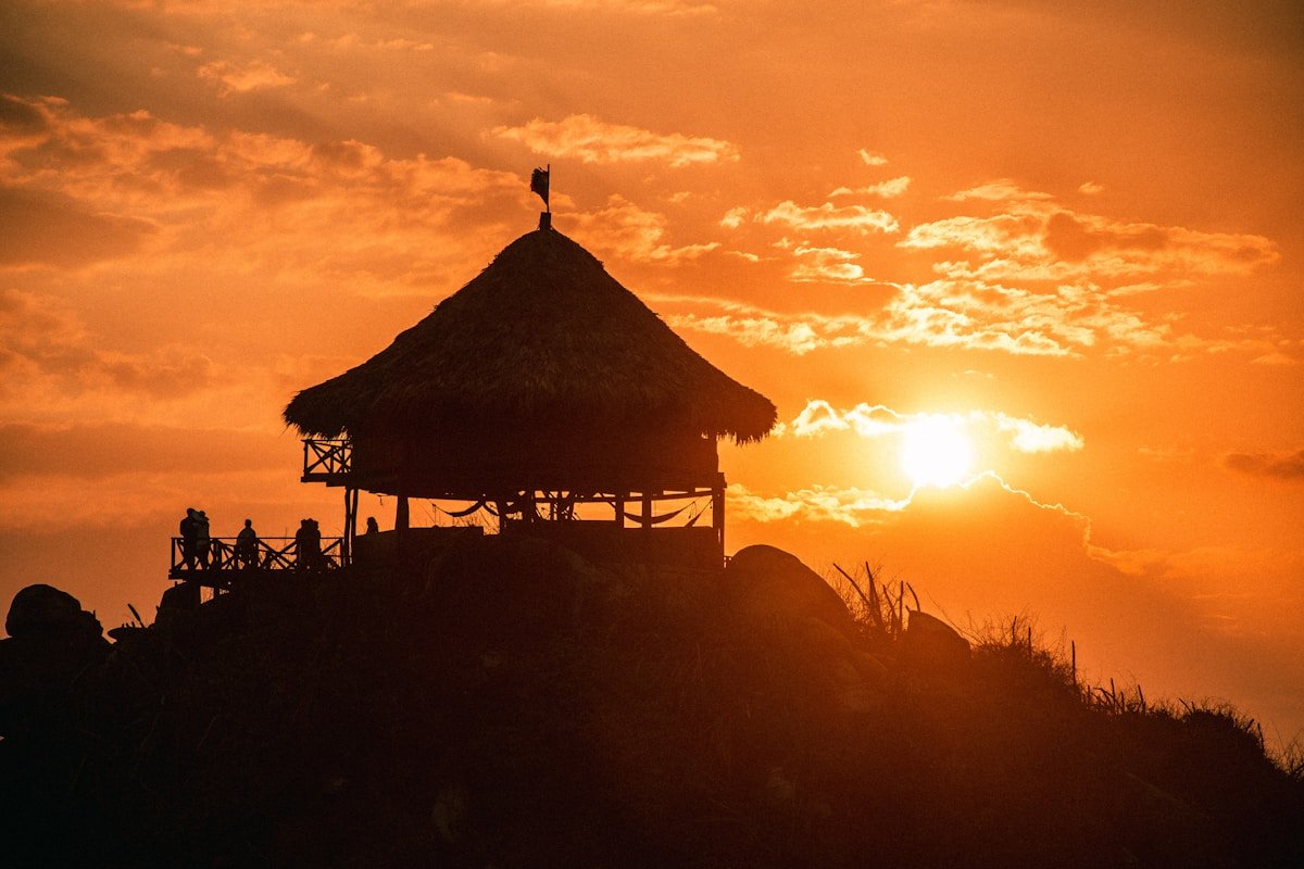Silhouettes of people at a wooden beach gazebo at sunset on the Santa Marta coast