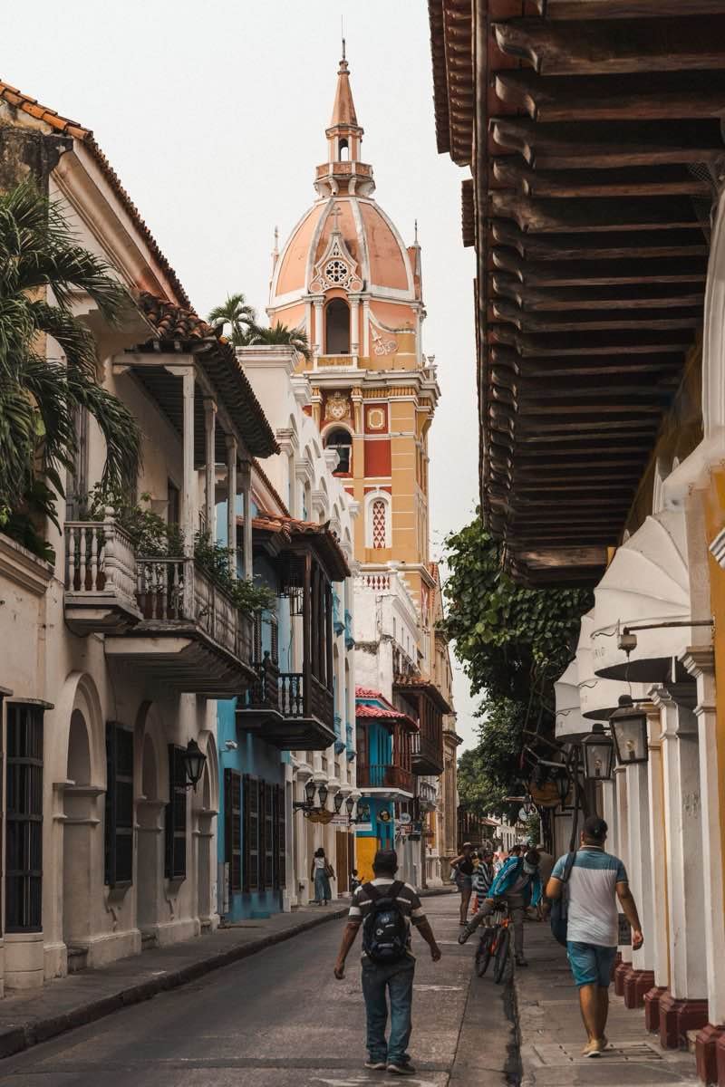 Pedestrians on a narrow street below the cathedral tower in Cartagena