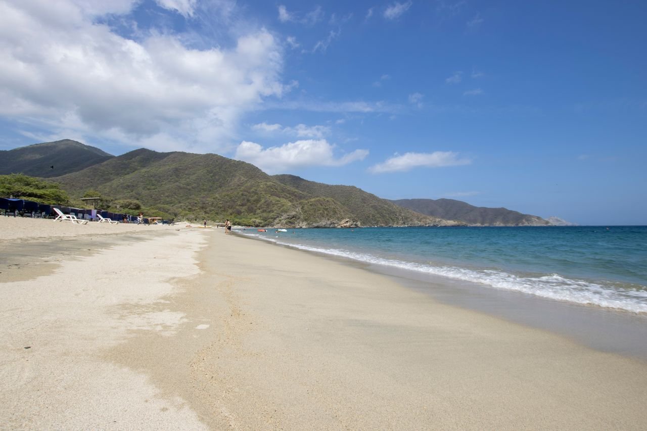 Long sandy beach with green mountains behind in Tayrona National Park