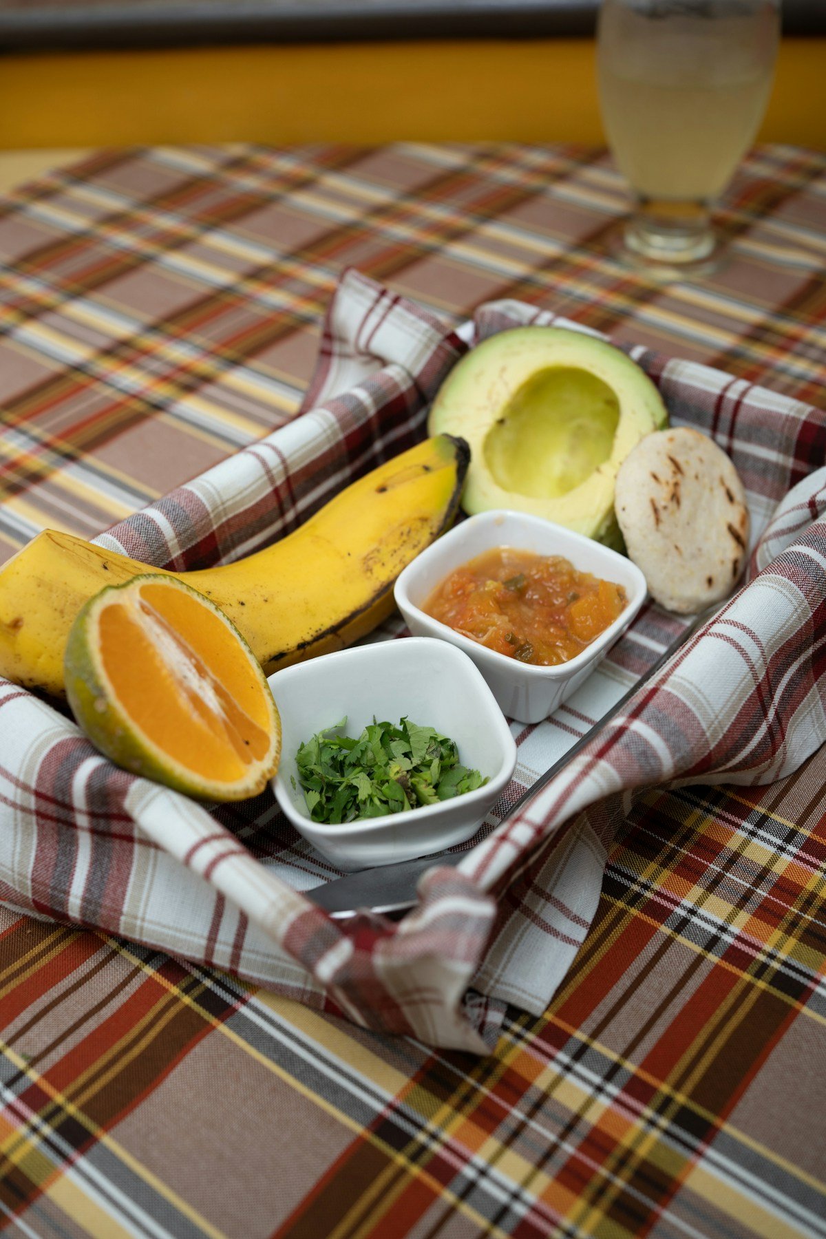 Traditional Colombian breakfast spread on a plaid tablecloth with arepa, avocado, banana, citrus and hogao salsa, Manizales