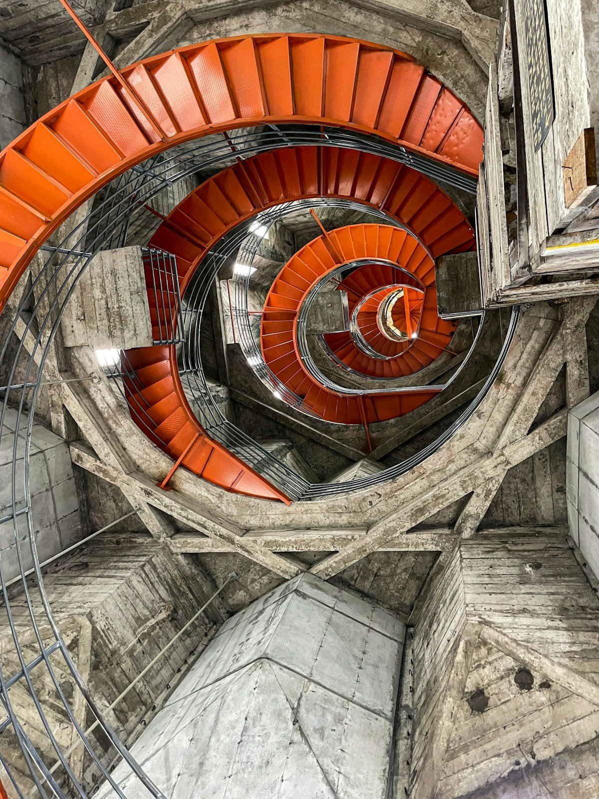 Looking up through the spiral staircase of Manizales cathedral, orange railings curving upward against grey concrete walls