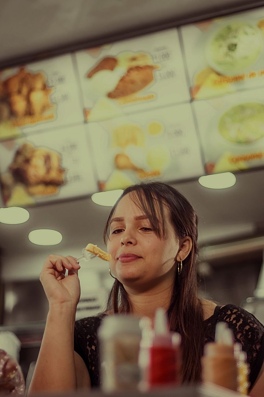 Woman eating at a Medellín restaurant with a bright Colombian fast food menu board in the background