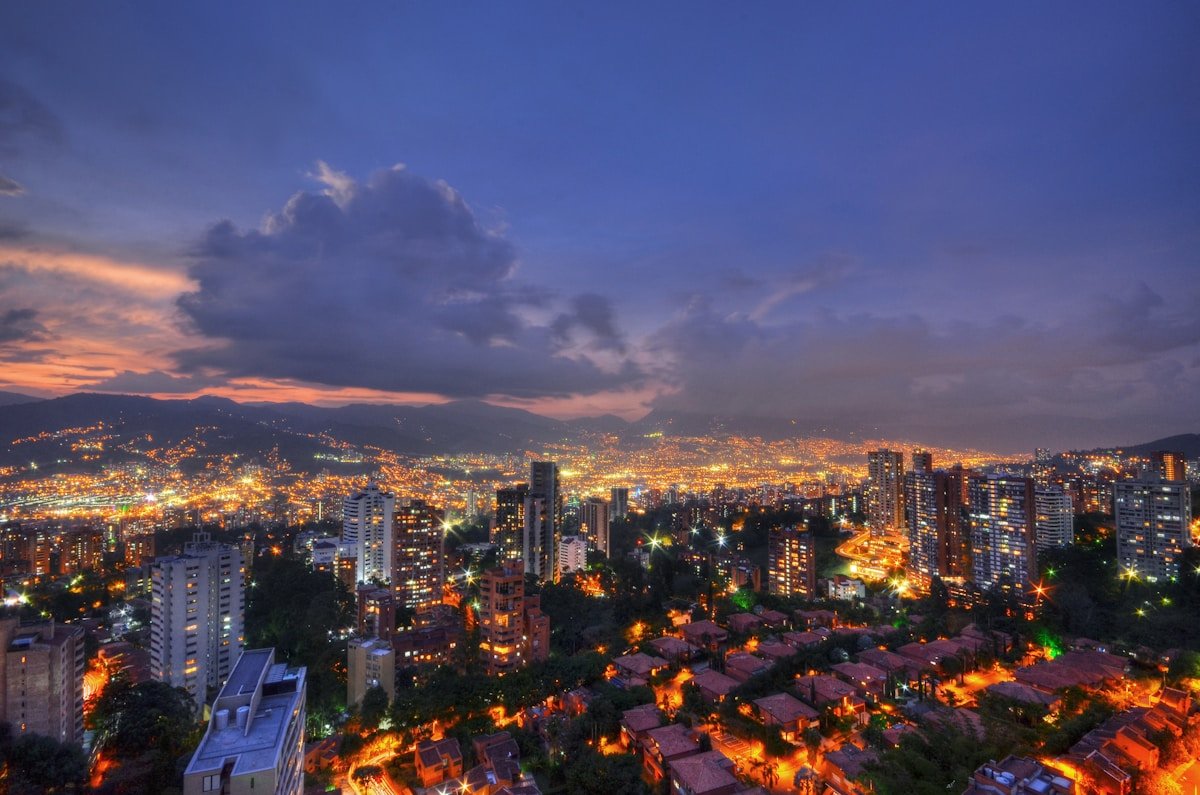 Medellin city panorama glowing with orange lights at dusk, the Andean hillside comunas rising on all sides