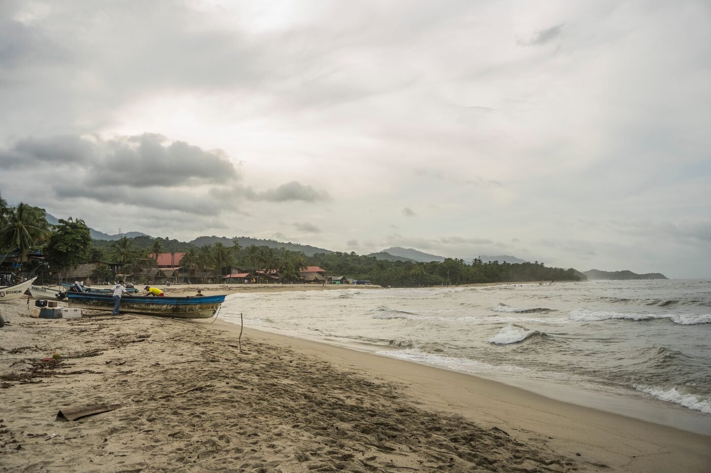 Sandy beach in Palomino, Colombia with fishing boats pulled up at the shore and palm-covered hills behind