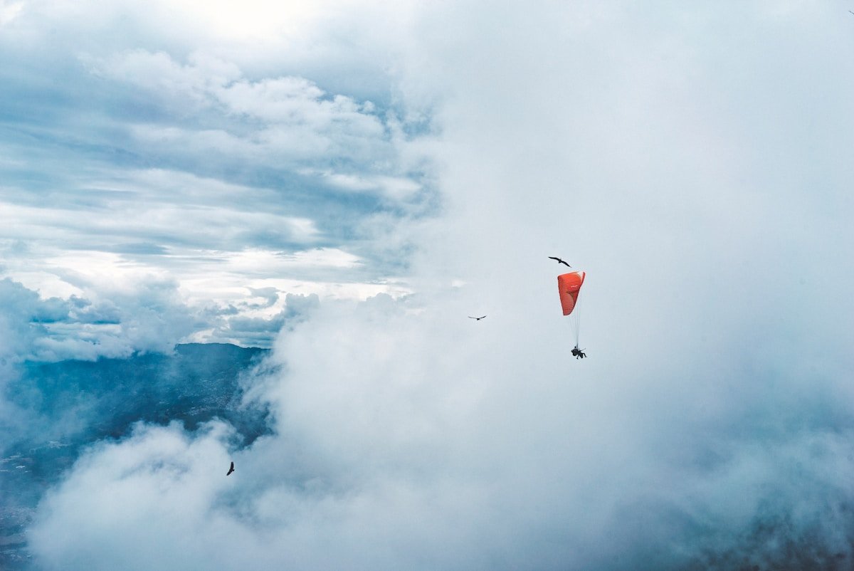 Paraglider with an orange canopy soaring above the cloud layer with Andean ridges visible through the mist near Medellin