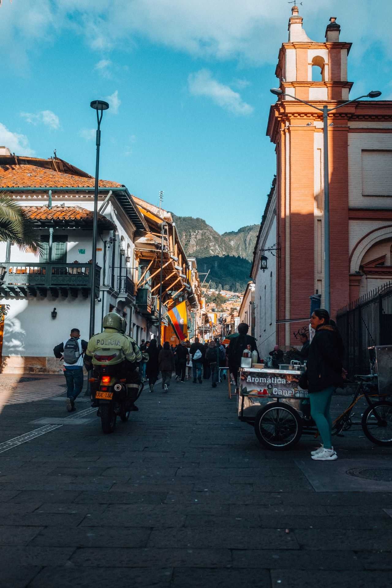 Pedestrian street in Bogota with a church, street vendor, and Colombian flag on a clear day