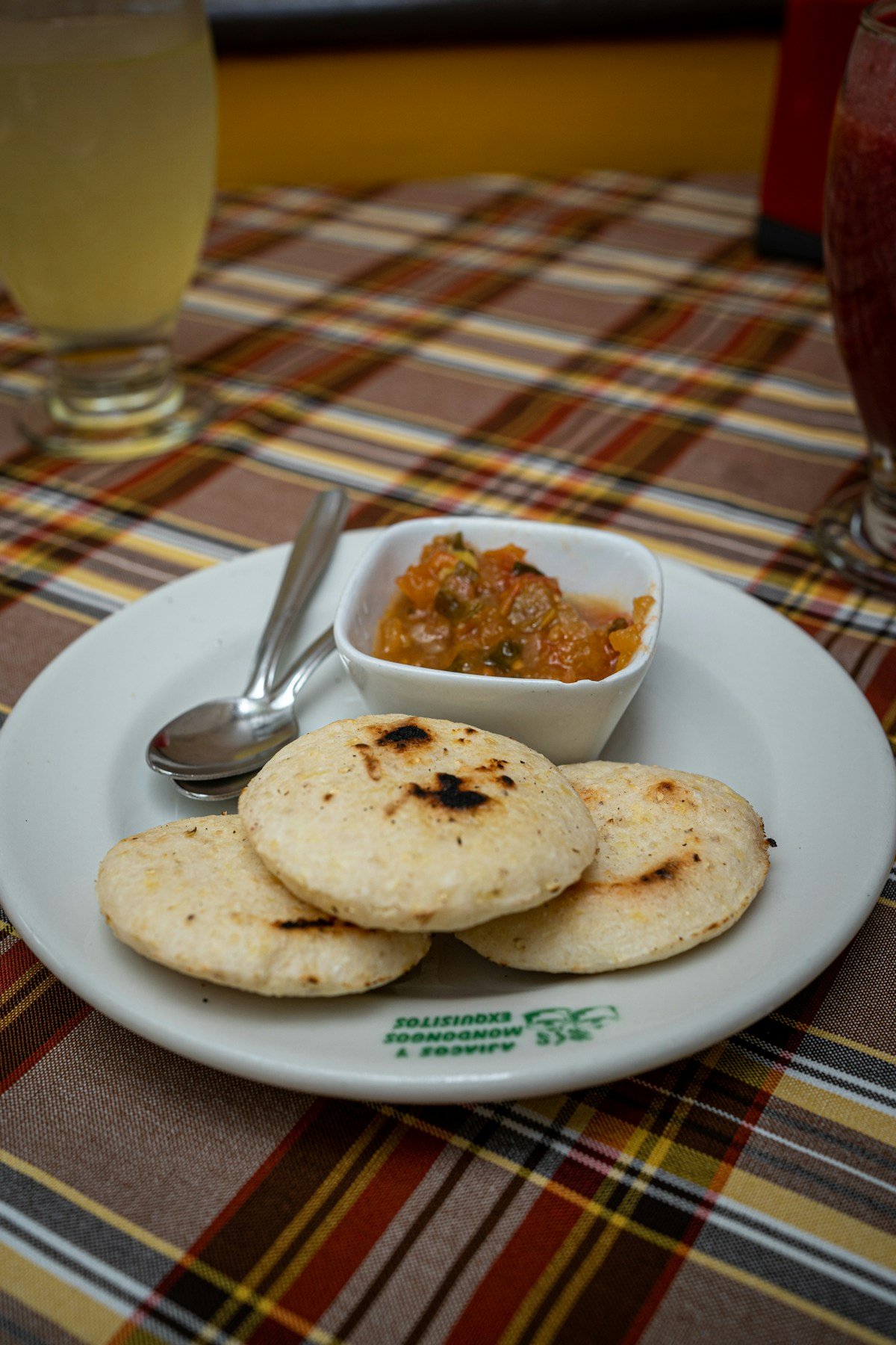 Arepas on a white plate served with salsa and fresh juice, a classic Colombian restaurant setting