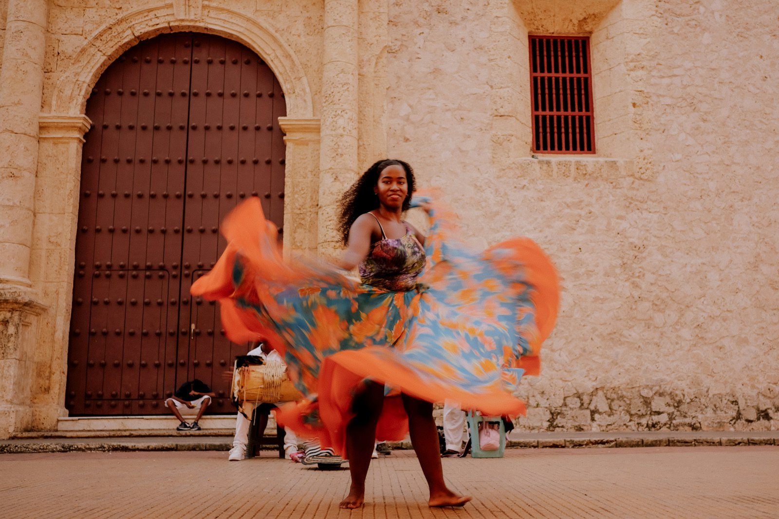 A woman in a bright orange and teal dress spinning while dancing in Cartagena, Colombia