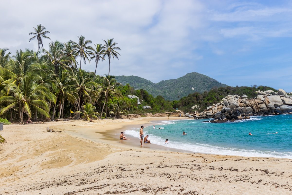 Palm-lined golden beach with turquoise Caribbean water and jungle-covered granite boulders at Tayrona National Park, Colombia