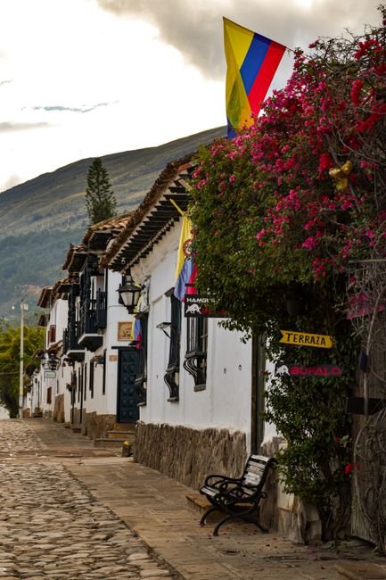 Cobblestone street in Villa de Leyva with a colonial whitewashed building, blue sky, and a mototaxi passing