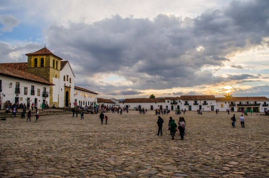 The vast cobblestone main plaza of Villa de Leyva at dawn, framed by whitewashed colonial buildings and a clear blue sky